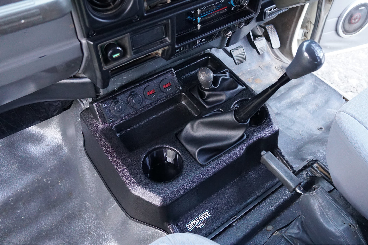 Close-up of a vehicle's center console with gear shift and cup holders.