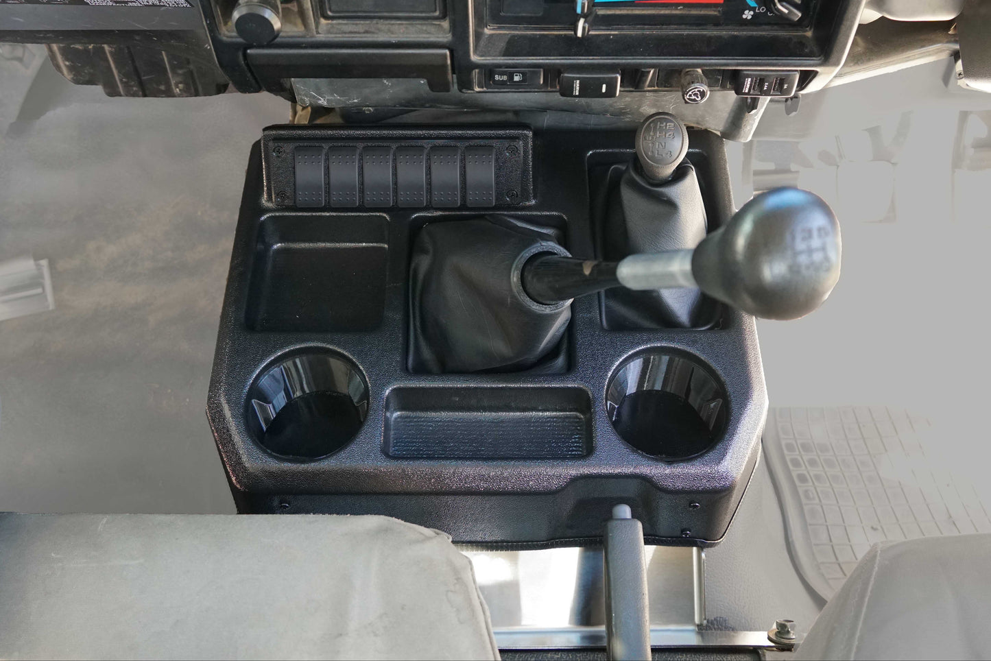 Close-up of a vehicle's dashboard and steering wheel area with a focus on the gear shift and cup holders.